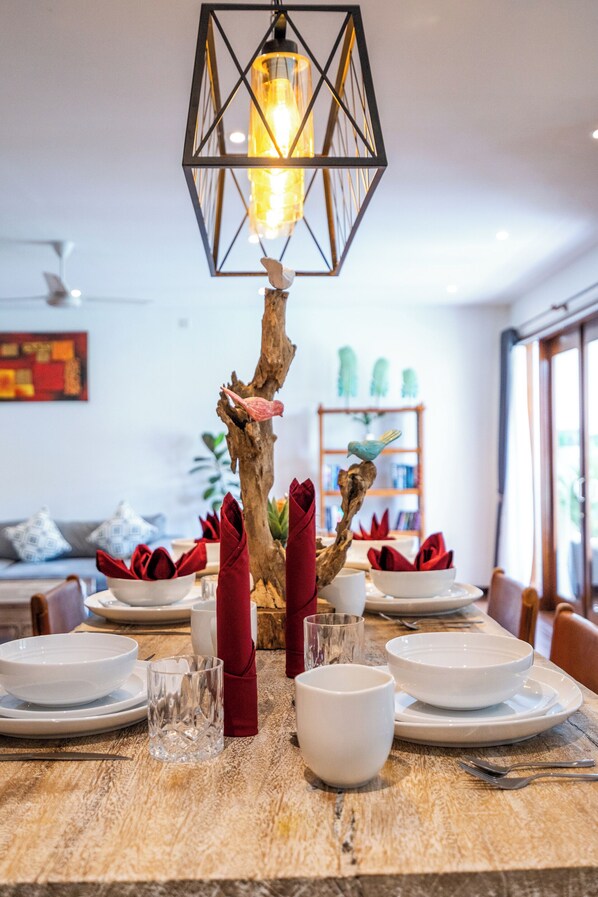 A dining table set with white plates, bowls, and glasses, a wooden branch centerpiece, and a hanging light fixture.