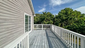 A wooden deck with a white railing, leading to a house with large windows.