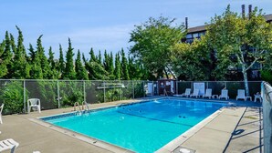 A rectangular swimming pool with a ladder, surrounded by a fence. There are lounge chairs and a small white chair near the pool.
