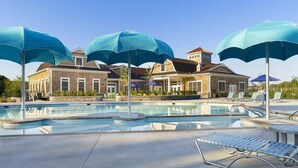 Een zwembadgedeelte met ligbedden en parasols, een gebouw met een bakstenen gevel, en een heldere lucht.