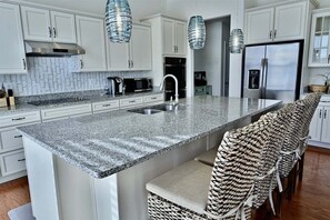 A kitchen with white cabinets, a granite countertop, stainless steel appliances, and woven chairs.