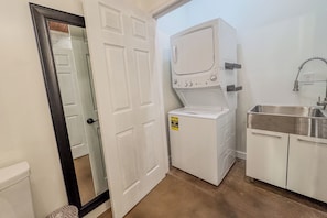 A laundry room with a front-loading washer and dryer, a sink, and a door leading to another room. - Cozy Farm Stay at Top Hat Equestrian.  Horse and pet friendly! (Fairhope)