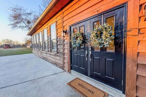 A wooden building with two black doors, a welcome mat, and two wreaths on the doors.