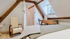 Un dormitorio con techo inclinado, un escritorio de madera, una silla y una cama.