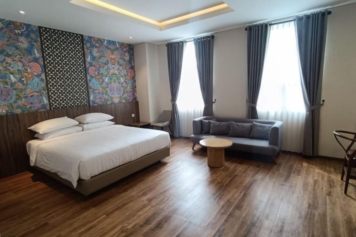 A modern hotel room with a large bed, a sofa, a small round table, and a decorative wall.
