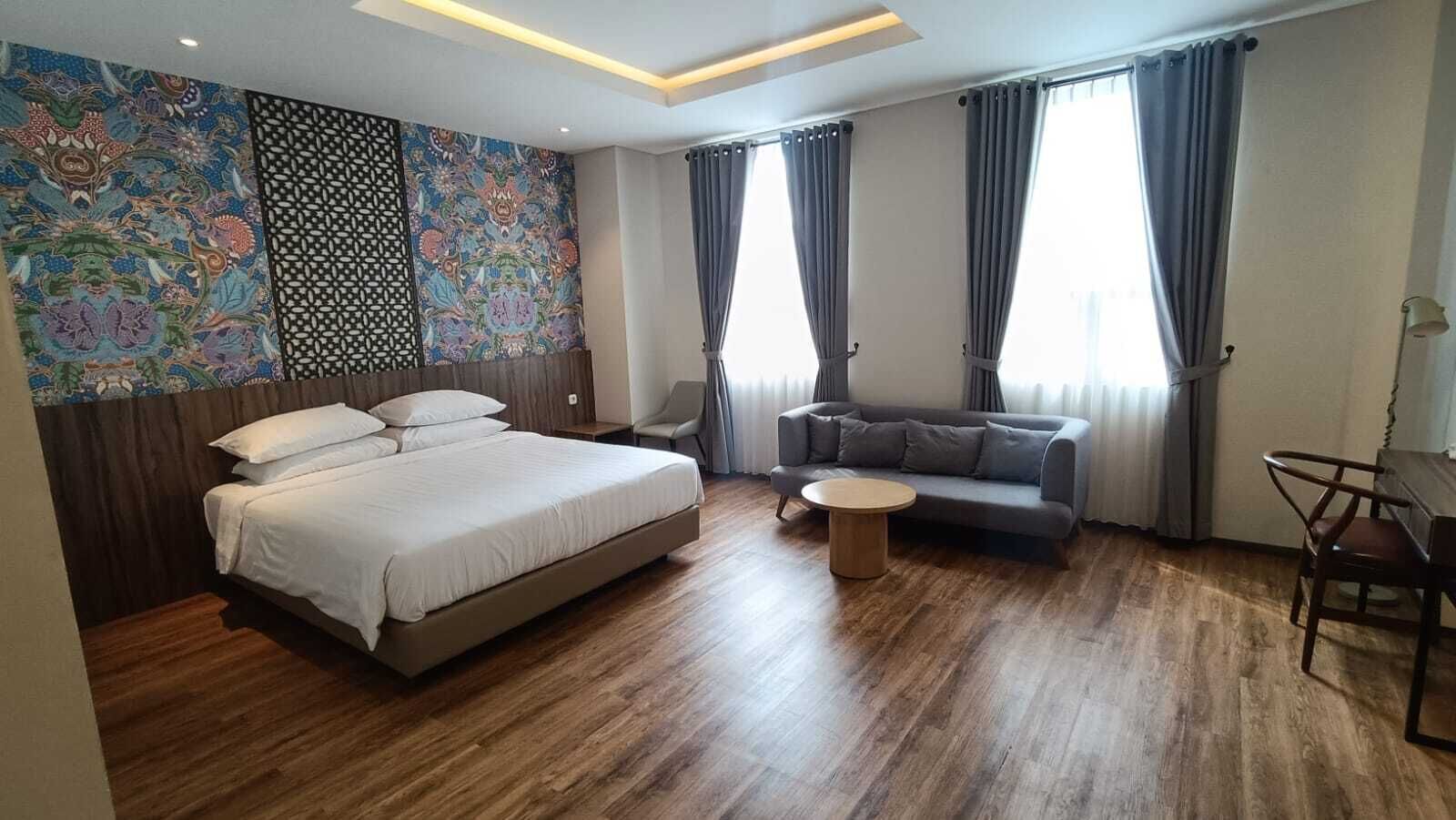 A modern hotel room with a large bed, a sofa, a small round table, and a decorative wall with intricate patterns.