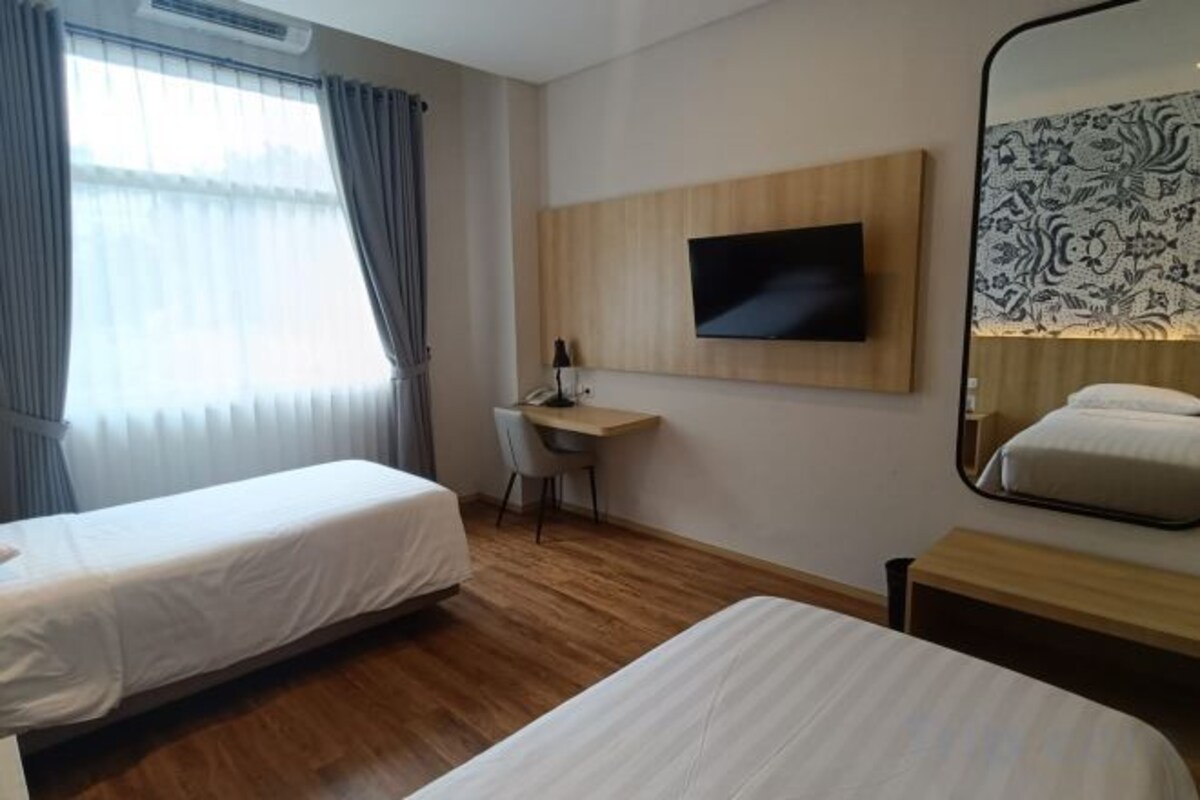 A hotel room with two beds, a desk, a chair, a TV, and a large mirror.