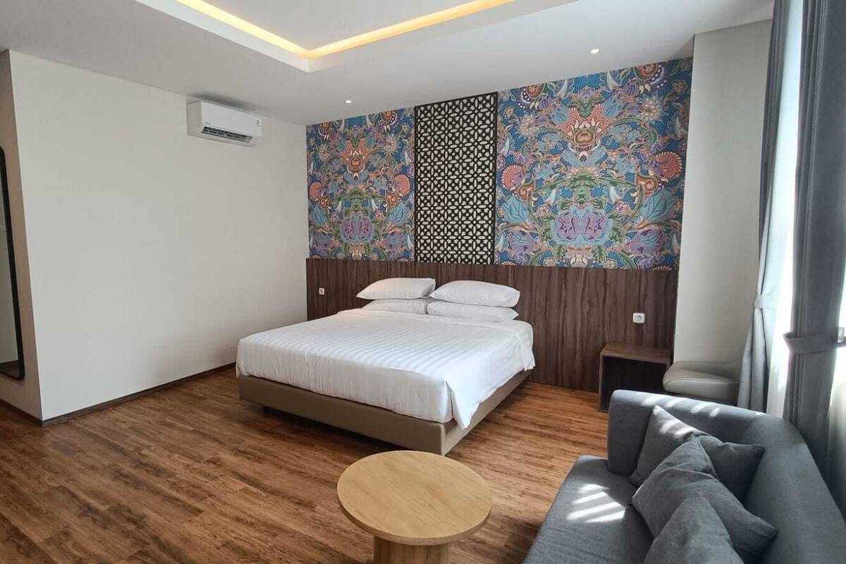 A modern hotel room with a large bed, a small round table, a sofa, and a decorative wall with intricate patterns.