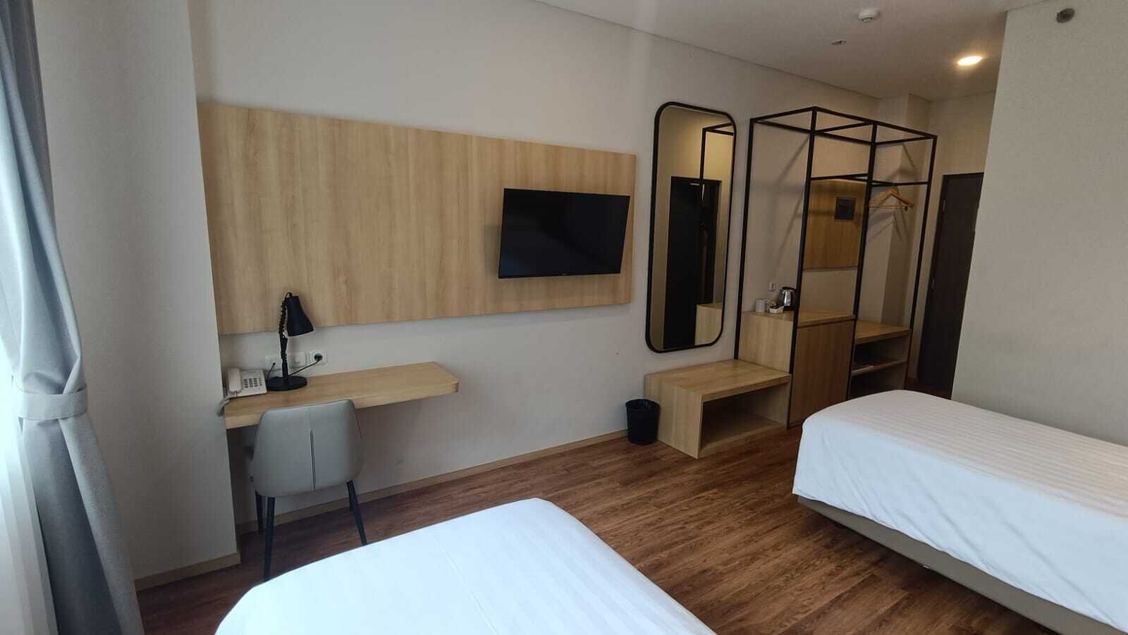 Een hotelkamer met twee enkele bedden, een bureau met stoel, een aan de muur bevestigde televisie en een grote spiegel.
