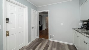 A hallway with a white door, a kitchen area with a countertop and cabinets, and a wooden floor. - Kenwood Keys 1 – Cozy Stay for 6 (Cincinnati)
