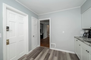 A hallway with a white door, a kitchen area with a countertop and cabinets, and a wooden floor. - Kenwood Keys 1 – Cozy Stay for 6 (Cincinnati)