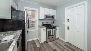 A compact kitchen with white cabinets, a black refrigerator, a microwave, a stove, and a sink. - Kenwood Keys 1 – Cozy Stay for 6 (Cincinnati)