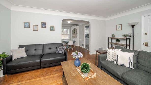 A modern living room with a black leather sofa, a wooden coffee table, and a grey sofa with patterned cushions. There are framed pictures on the wall and a small plant on the coffee table. - Kenwood Keys 1 – Cozy Stay for 6 (Cincinnati)