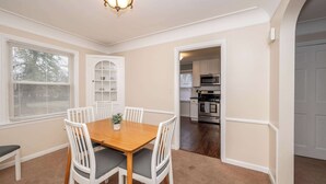 A dining area with a wooden table and white chairs, a built-in bookshelf, and a kitchen visible through an open doorway. - Kenwood Keys 2 – Stay for 6! (Cincinnati)