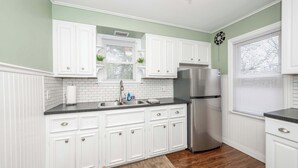 A kitchen with white cabinets, a stainless steel refrigerator, and a window with blinds. - Kenwood Keys 2 – Stay for 6! (Cincinnati)