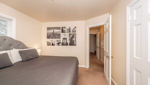 A bedroom with a large bed, a cityscape wall art, and a hallway leading to another room. - Kenwood Keys 2 – Stay for 6! (Cincinnati)