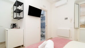 A bedroom with a bed, a TV, a shelf, a door to the bathroom, and a radiator. - Lucia Cottage BB (Massa Lubrense)