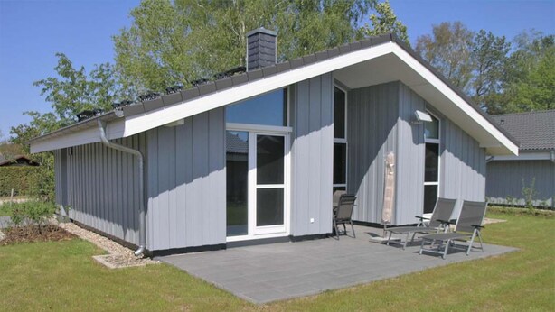 A modern house with a flat roof, large sliding glass doors, and a patio with outdoor furniture. - Ferienhaus mit Sauna im Ferienpark Mirow (Mirow)
