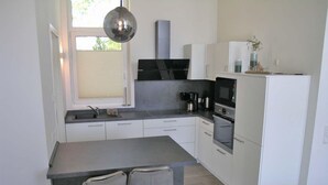 A modern kitchen with white cabinets, a central island with two chairs, a built-in oven, and a hanging light fixture. - Ferienhaus mit Sauna im Ferienpark Mirow (Mirow)