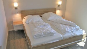 A neatly made bed with white bedding in a modern room with wooden flooring and two wall-mounted nightstands. - Ferienhaus mit Sauna im Ferienpark Mirow (Mirow)