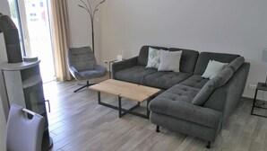 A modern living room with a grey sectional sofa, a wooden coffee table, a grey armchair, and a tall floor lamp. - Ferienhaus mit Sauna im Ferienpark Mirow (Mirow)