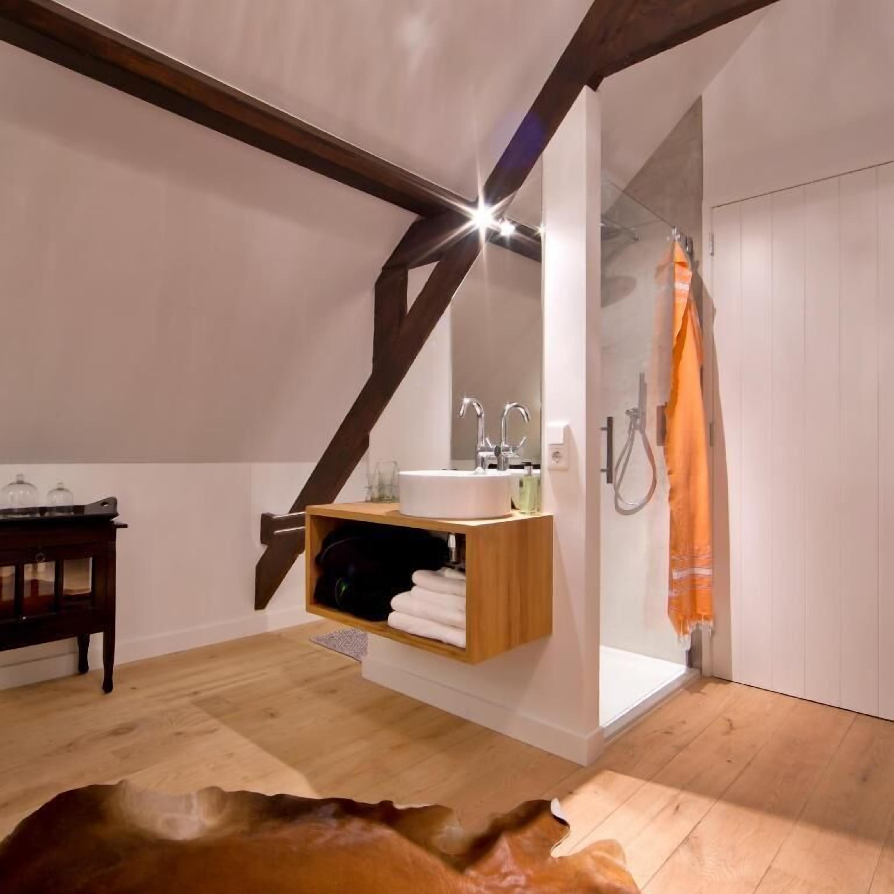 Une salle de bain moderne avec un meuble-lavabo en bois, une étagère suspendue et une douche agrémentée d’une serviette orange.