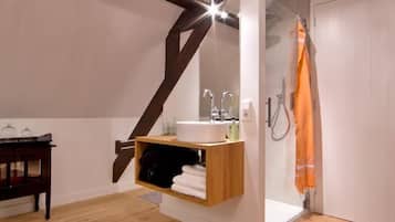 A modern bathroom with a wooden vanity, a hanging shelf, and a shower with an orange towel.