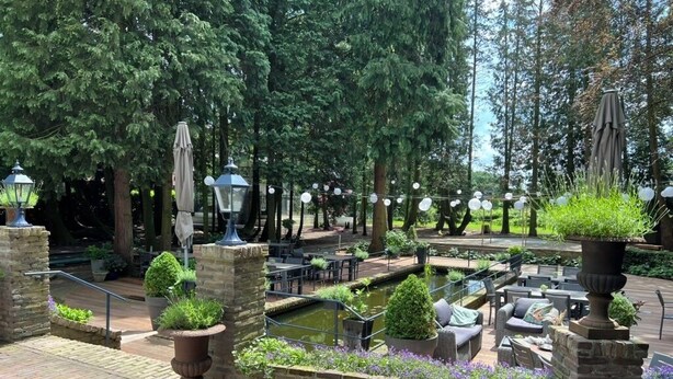 An outdoor patio area with brick flooring, seating arrangements, a small pond, and surrounding greenery. - Villa Polder – Boutique Hotel near Eindhoven (Gemert)