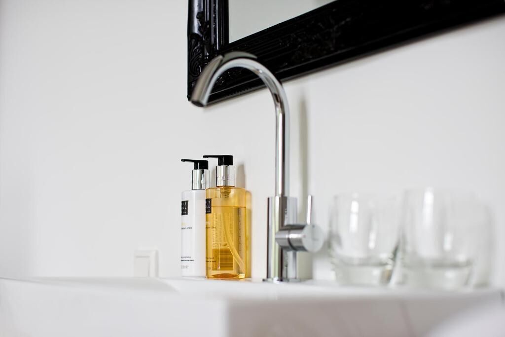 Un lavamanos de baño con un grifo moderno, dos botellas de jabón líquido y tres vasos de vidrio sobre la encimera.