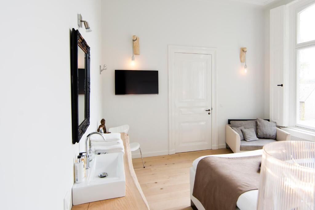 Een moderne slaapkamer met een witte deur, een wandtelevisie, een nachtkastje en een bed met een bruine deken.