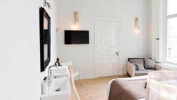 Een moderne slaapkamer met een witte deur, een wandtelevisie, een nachtkastje en een bed met een bruine deken.