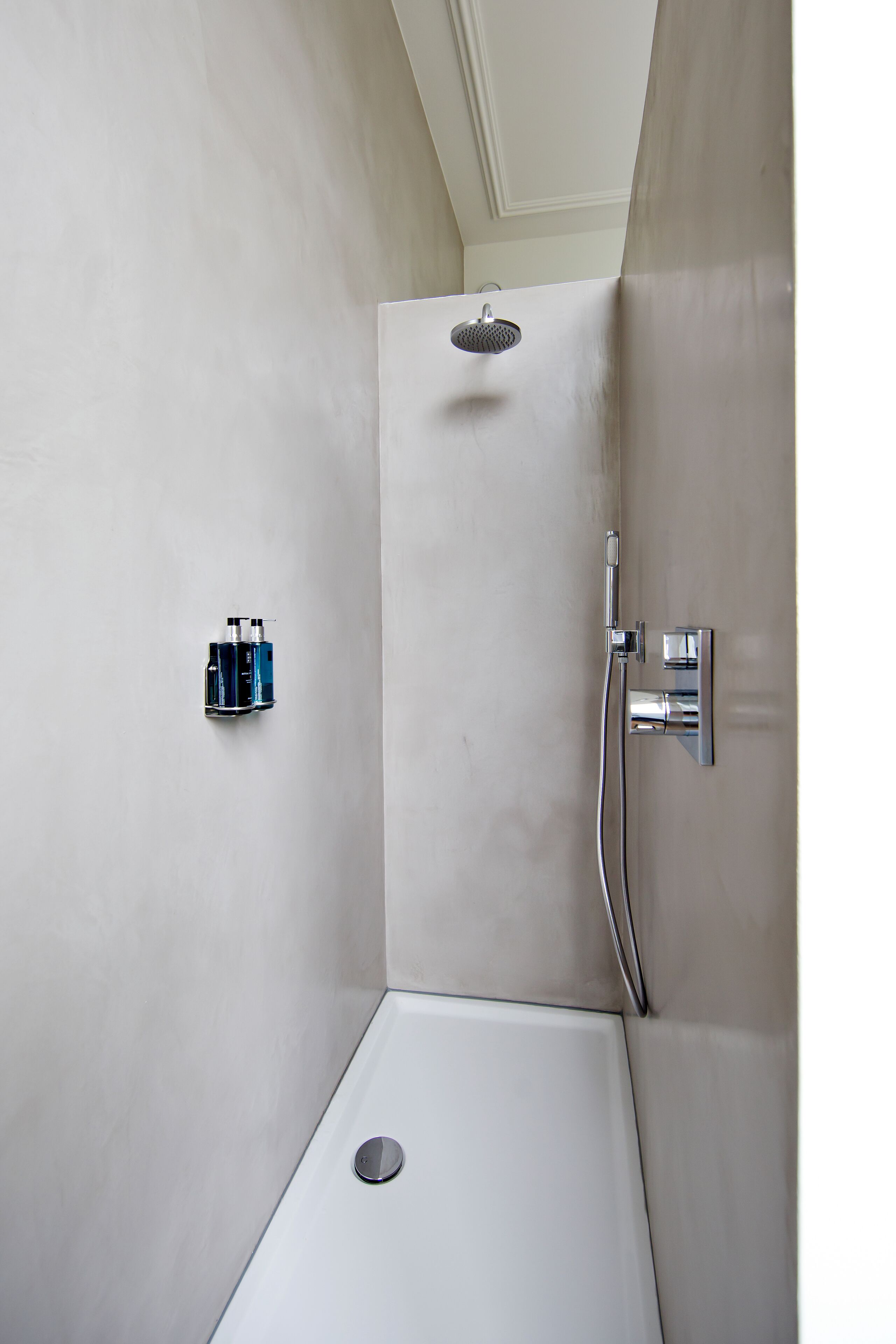 A small, white shower area with a handheld showerhead and a wall-mounted faucet.