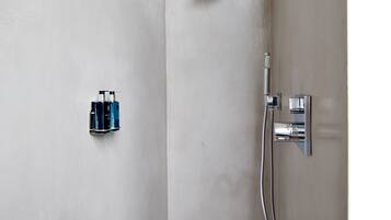 A small, white shower area with a handheld showerhead and a wall-mounted faucet.