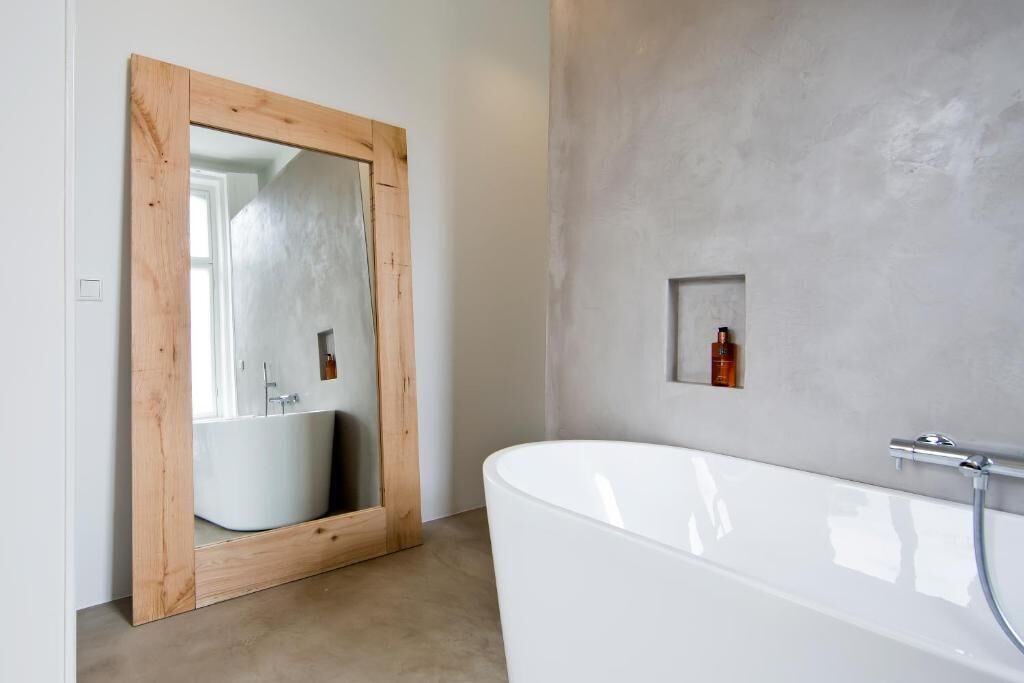 A modern bathroom with a freestanding bathtub, a wooden-framed mirror, and a small shelf with toiletries.