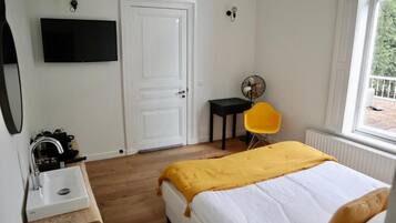 A bedroom with a bed, a bedside table with a sink, a TV mounted on the wall, a door, and a window.