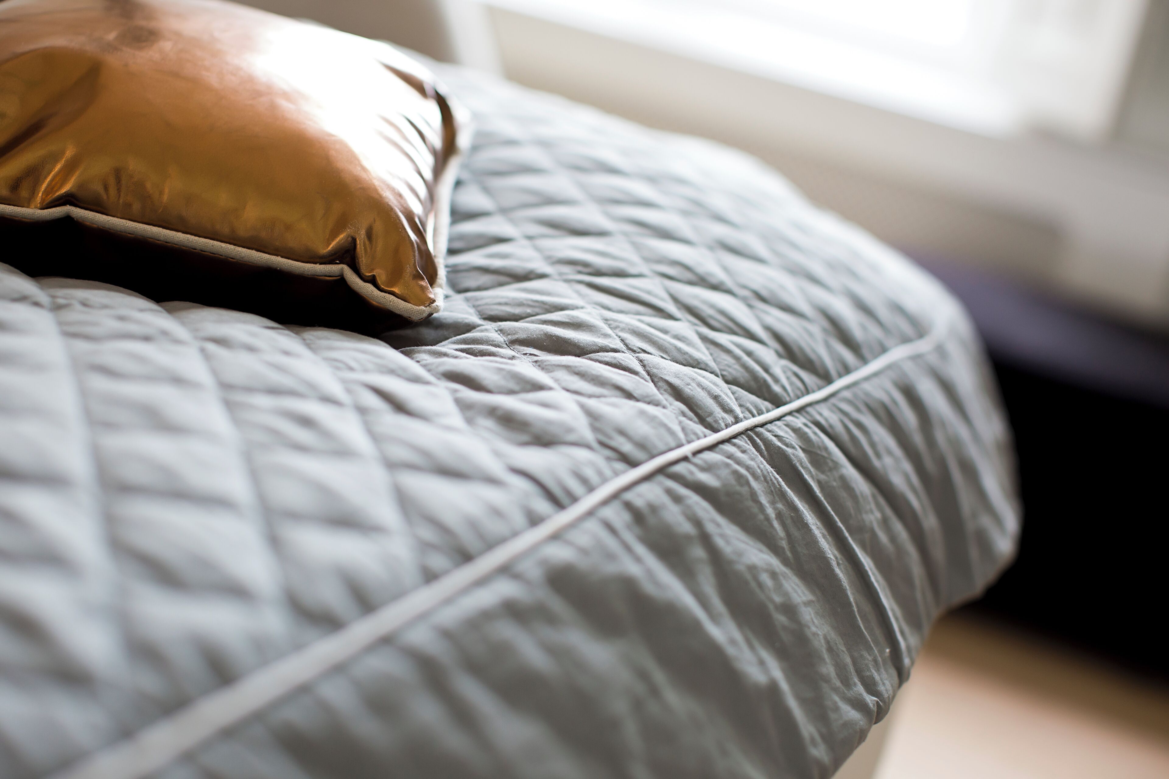 Un letto con una coperta grigia trapuntata e un cuscino dorato.