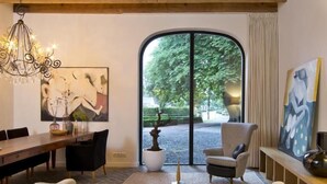A modern living room with a sofa, a dining table, a chandelier, and a large window with a view of greenery. - Villa Polder – Boutique Hotel near Eindhoven (Gemert)
