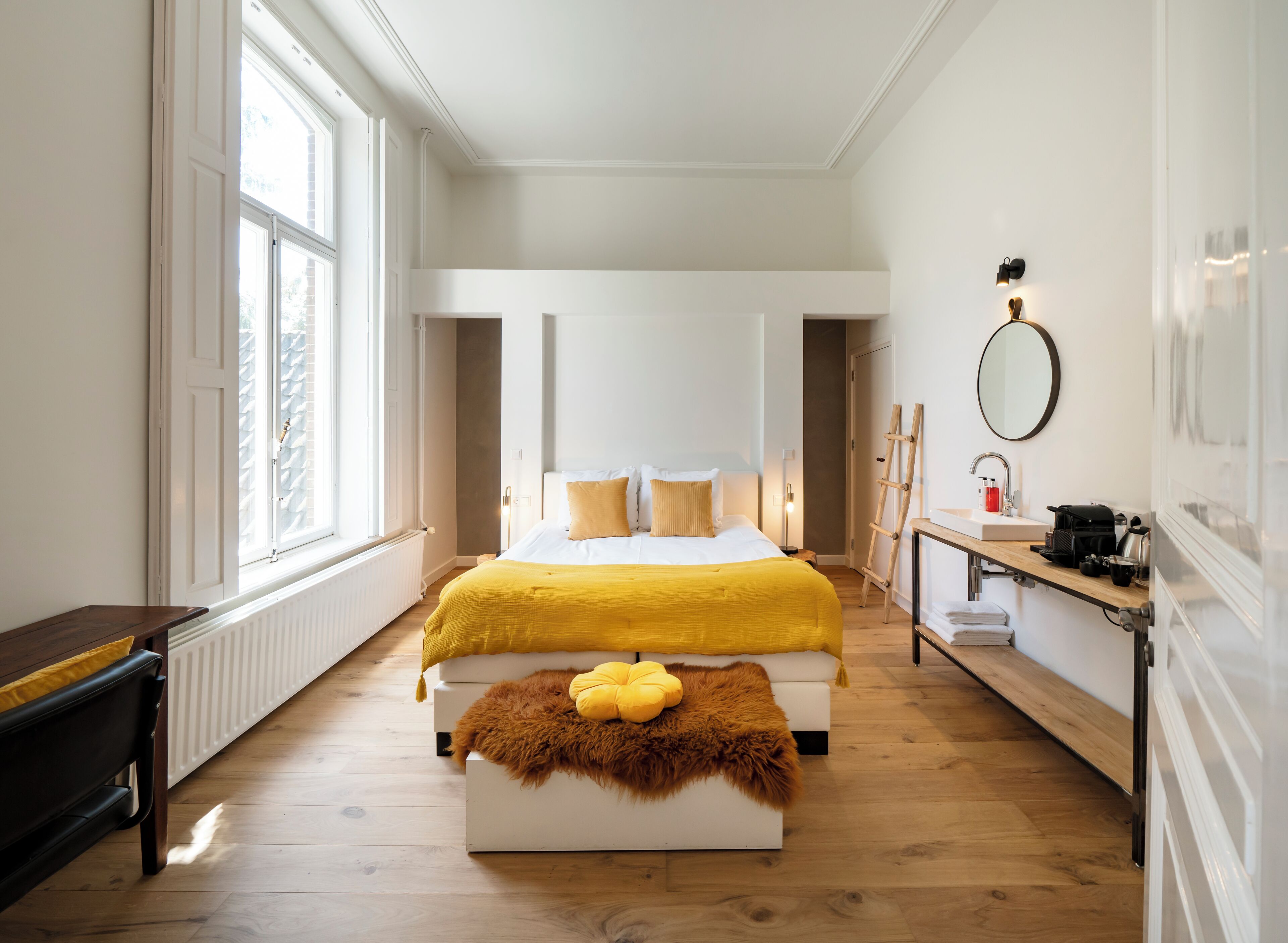 A bedroom with a large bed, a wooden bench, a small table with a mirror, and a radiator.