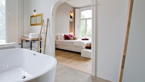 A modern bathroom with a freestanding bathtub, a vanity with a mirror, and a cozy seating area with a sofa and pillows. - Villa Polder – Boutique Hotel near Eindhoven (Gemert)