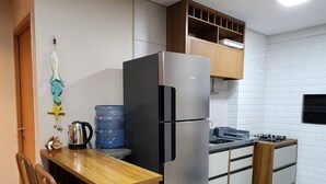 Een compacte keuken met een houten eettafel, stoelen, een roestvrijstalen koelkast, een gasfornuis en een waterdispenser.