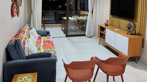 Een woonkamer met een bank, twee stoelen, een televisie en een eethoek met een tafel en stoelen.