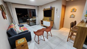 Een moderne woonkamer met een bank, twee fauteuils, een houten eettafel en een tv op een houten kast.