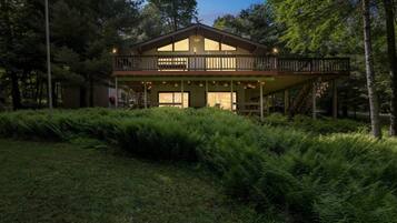 A two-story wooden house with a balcony, surrounded by dense ferns and trees.