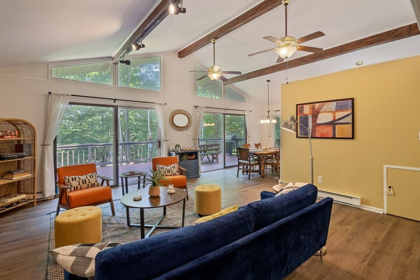 A spacious living room with a large sofa, a dining table, and a balcony with a view of trees.