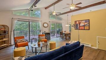 A spacious living room with a large sofa, a dining table, and a balcony with a view of trees.