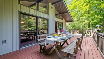 An outdoor deck with a wooden table and benches, surrounded by a railing and trees.