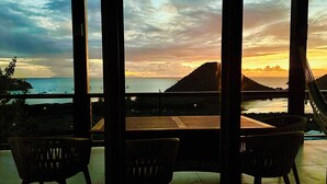 Una terrazza con tavolo e sedie che si affaccia su un panorama mozzafiato al tramonto sul mare.