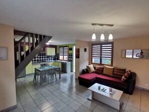 A living room with a sofa, coffee table, and a dining area with a table and chairs. - Gîte Les Arches ***, sleeps 4, fully equipped, 10 km from the ocean (Méneslies)