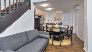 A compact living space with a gray sofa, a dining table with chairs, a kitchen area, and a staircase. - Fox Hotel Palais Des Congres (Montréal)