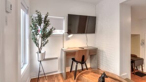 Een moderne kamer met een houten bureau, een stoel, een wandtelevisie, een potplant en een klein beeldje.